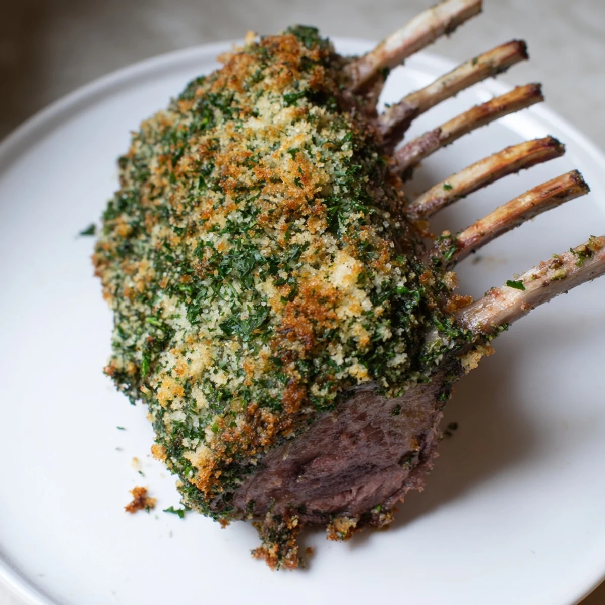 A beautifully plated herb crusted rack of lamb, with savory herb crust and tender, pink meat.