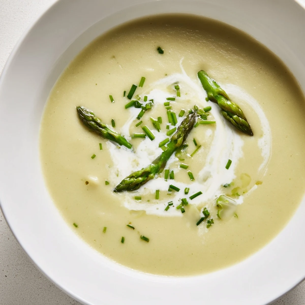 Smooth, velvety creamy asparagus soup swirled with cream, garnished with fresh chives, looks delicious.