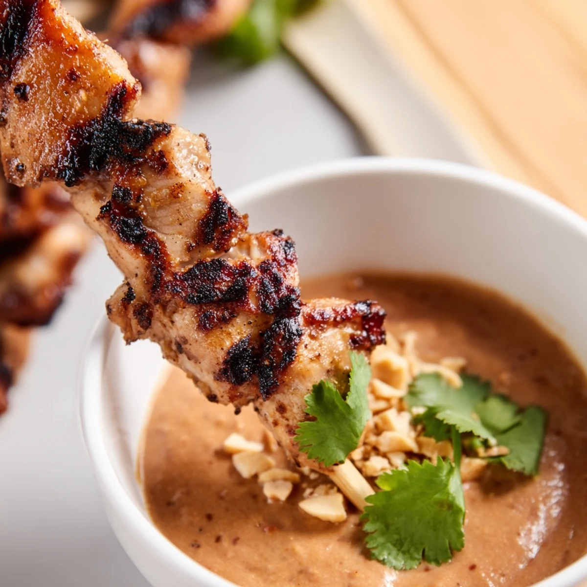 Des brochettes de poulet satay grillées avec sauce aux arachides sur une planche en bois.