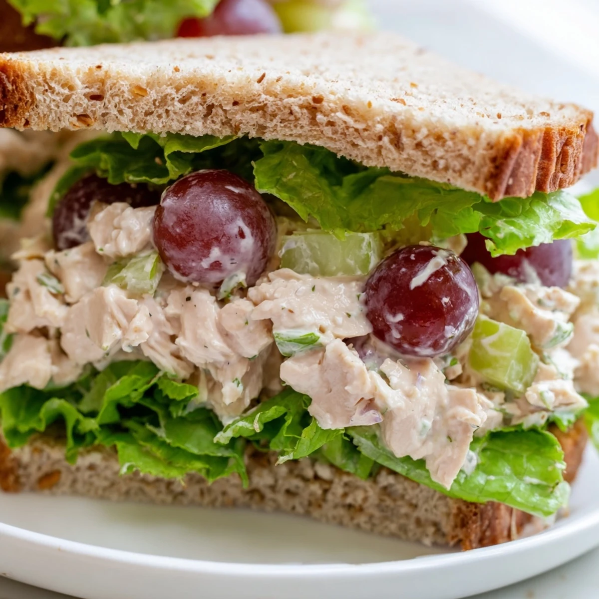 Morceaux tendres de poulet et raisins rouges sucrés dans une salade crémeuse, servis sur un sandwich avec un brin de céleri.