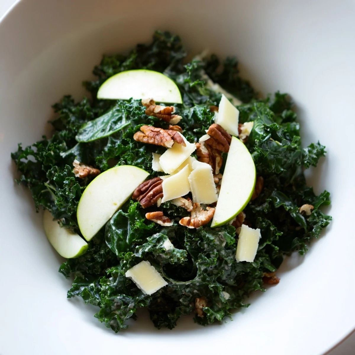 Close-up of a vibrant Winter Kale Salad with Apple and Cheddar, featuring massaged kale, crisp apple slices, sharp cheddar cubes, and toasted pecans on a rustic wooden table.