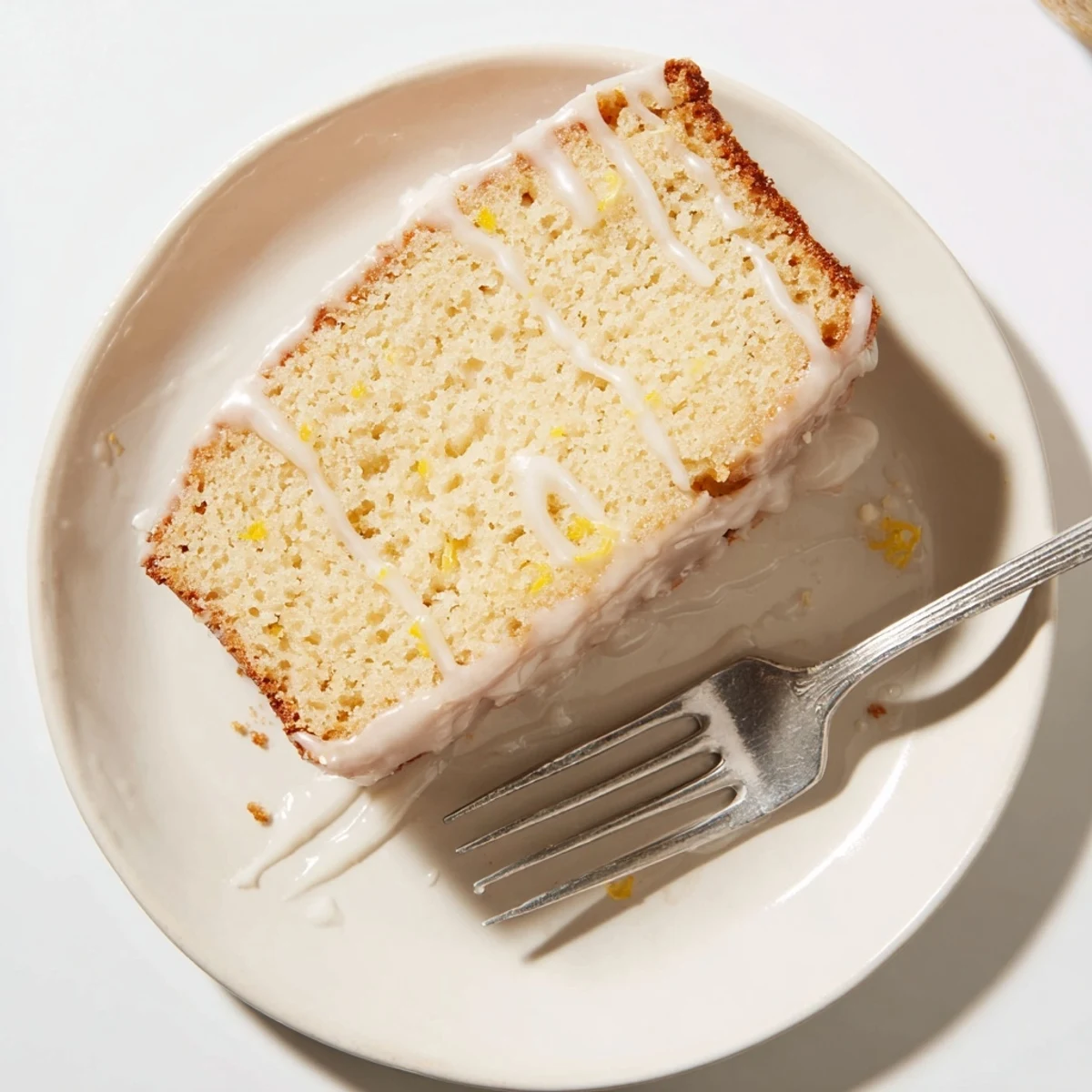 Une tranche de pain au citron glacee, avec une crumb texture humide et des zestes de citron frais sur le dessus, parfaite pour le petit-déjeuner ou l'heure du thé.