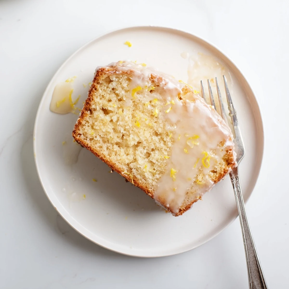 Coupe transversale d'un pain au citron montrant la mie tendre et humide, avec une glace au citron éclatante et des zestes sur le dessus.