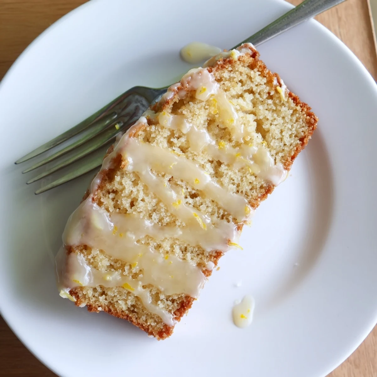 Gros plan sur une tranche de lemon bread loaf avec une drizzle de glace au citron qui coule, servie avec une tasse de thé Earl Grey.