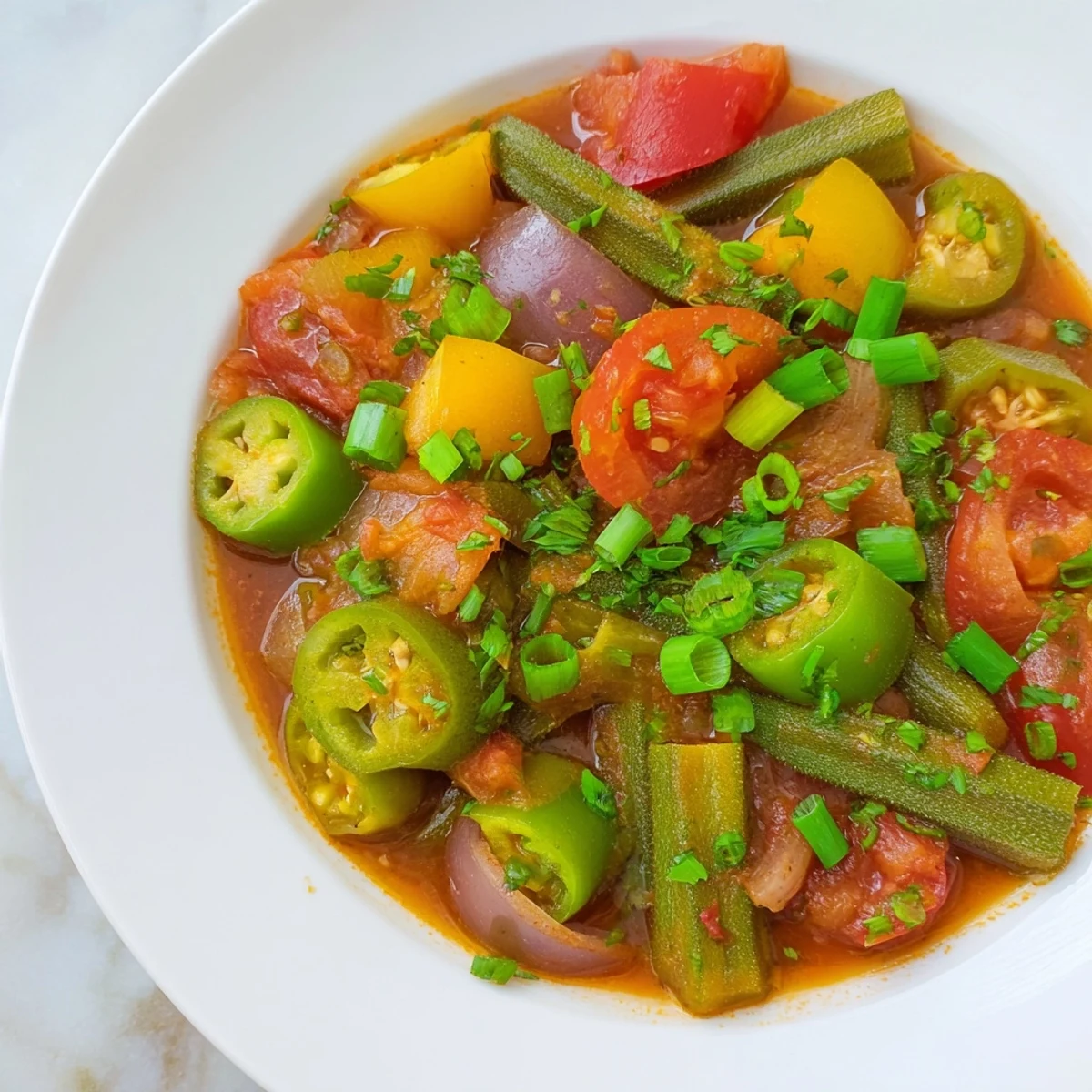 Okra and vegetable Creole gumbo simmering in a Dutch oven, with tender okra slices, diced peppers, and vibrant tomatoes in a rich broth.