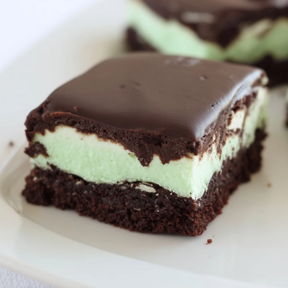 Un plat élégant de brownies Shamrock Mint Brownies au chocolat fondu, garni d’une crème à la menthe rafraîchissante et d’une ganache.