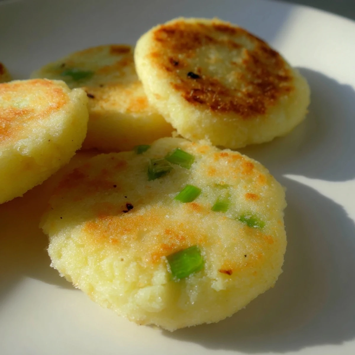 Cakes de pommes de terre irlandais aux oignons verts, croquants à l'extérieur et moelleux à l'intérieur, présentés sur une assiette blanche.