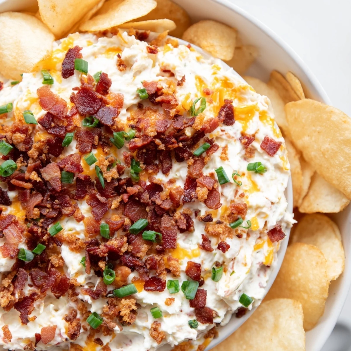 Un bol de Loaded Baked Potato Dip aux copeaux de bacon et aux oignons verts frais, servi avec des chips de pommes de terre croustillantes.