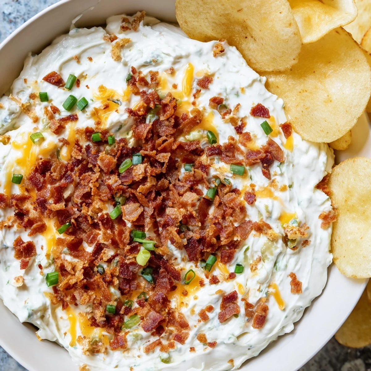 Une assiette de dip inspiré des pommes de terre au four chargées, garnie de bacon croquant et de fines herbes pour un goûter convivial.