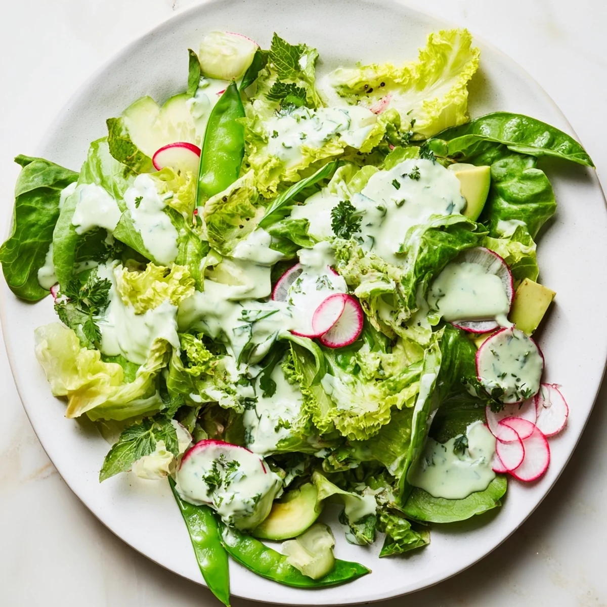Fresh Green Goddess salad with snap peas, radishes, and herbs on a plate.