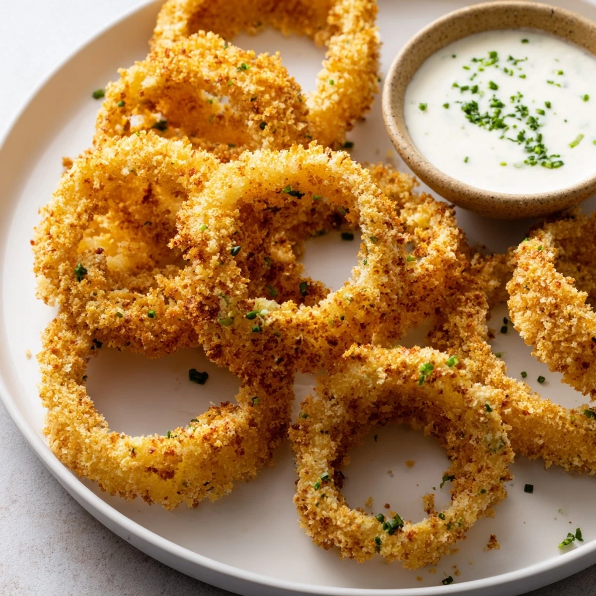 Freshly baked Crispy Baked Onion Rings with Ranch showing golden crumbs and a generous bowl of herby ranch for dipping.