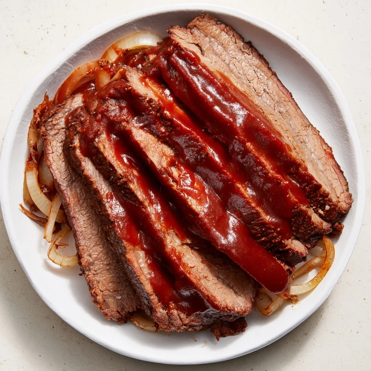 Slow cooked beef brisket with BBQ sauce sliced thin, juicy strands shown on a cutting board with rich sauce drizzled over.