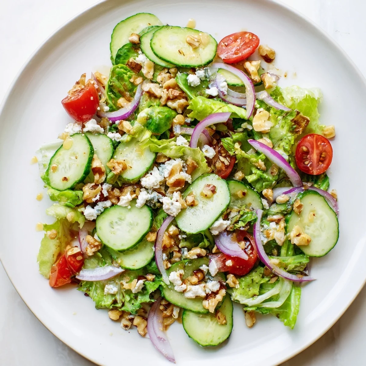 Fresh Spring Mix Salad with Vinaigrette topped with crumbled feta, halved cherry tomatoes, and sliced cucumber on a wooden serving board.