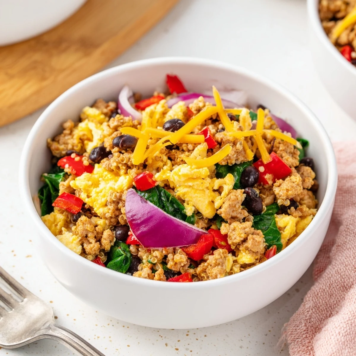 Colorful meal prep breakfast bowl featuring eggs, sausage crumbles, black beans, and fresh vegetables over fluffy quinoa base