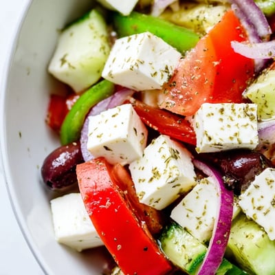 Assiette de Greek Salad with Kalamata Olives, Cucumber, and Feta avec feta crémeuse et olives noires Kalamata sur un fond de verdure.
